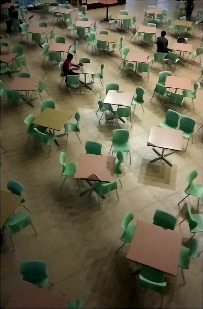 Empty cafeteria with green chairs and tables arranged in grid-like pattern, resembling a render.