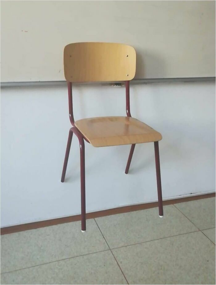 Wooden chair seemingly floating against a classroom wall, resembling a bad render.