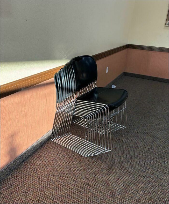 Stack of black chairs in a room, appearing like bad renders against a plain wall.