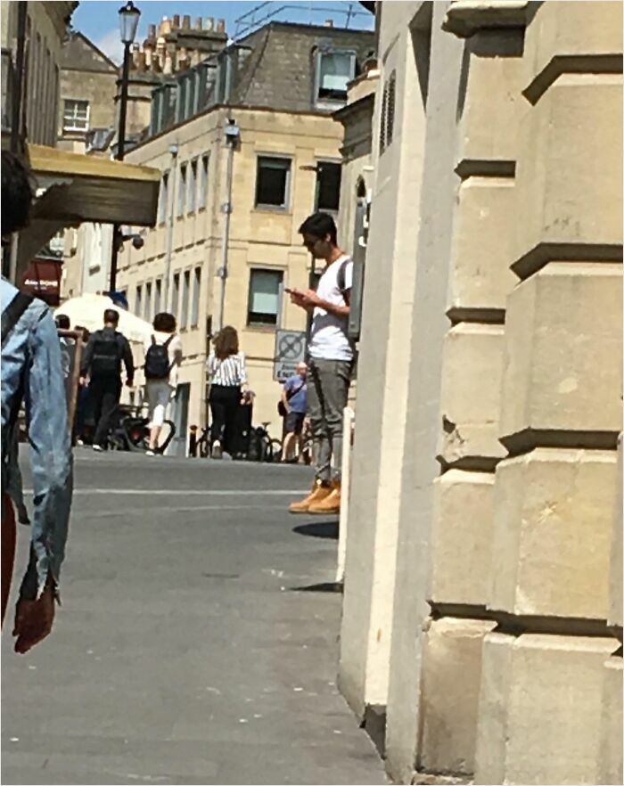 Street scene with a man standing against a building, resembling a bad render due to shadows and angles.