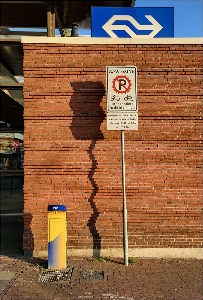 A sign casting a shadow resembling a bad render on a brick wall, with a railway station symbol above.