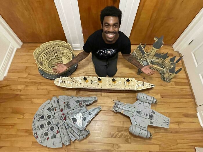 Person showcasing impressive cool LEGO builds, including iconic structures and vehicles, on a wooden floor.