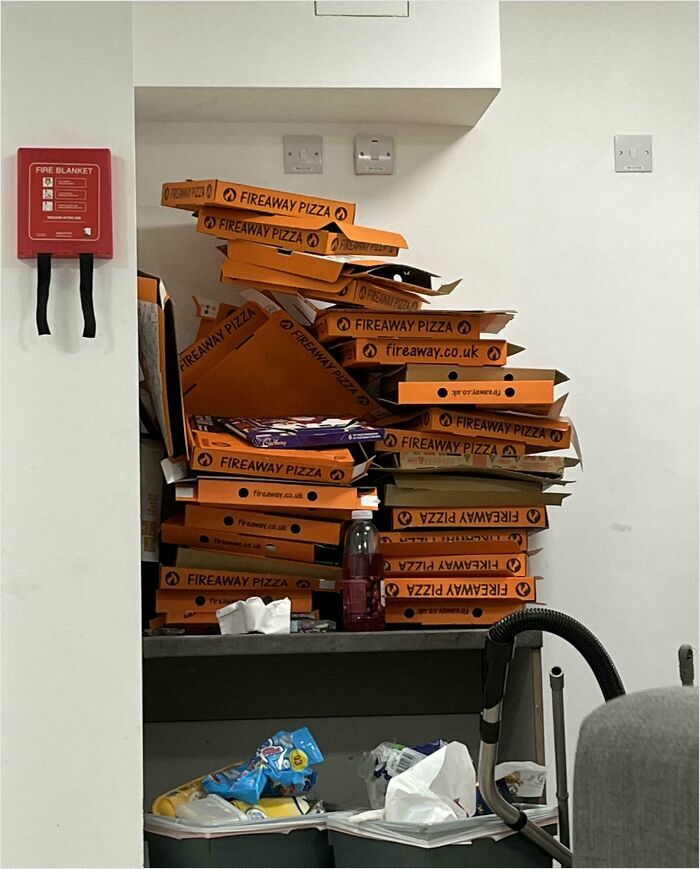 Pizza boxes stacked high in messy room, overfilled trash, illustrating horrible roommates.