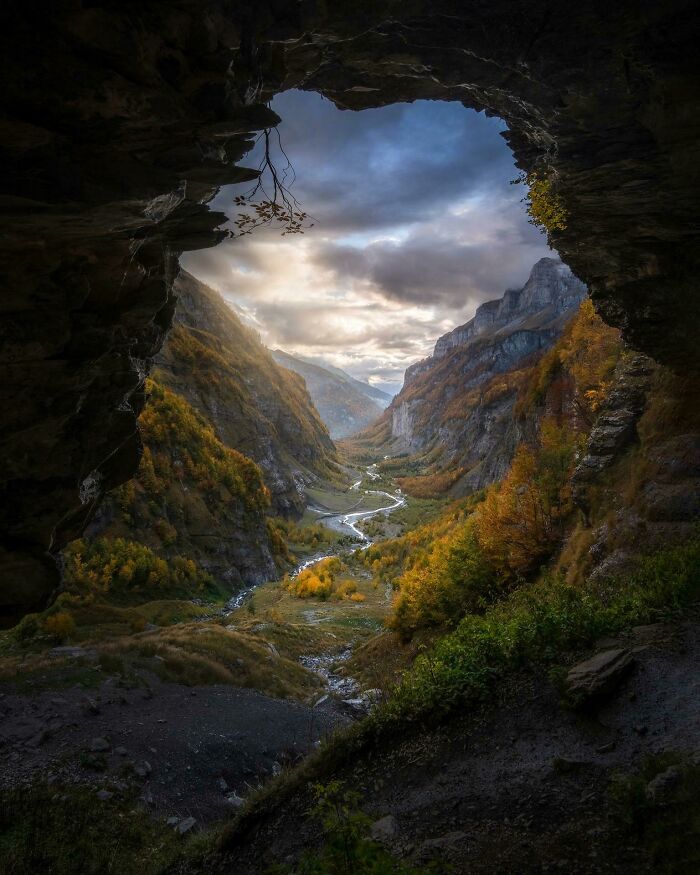 Incredible World Photos: Breathtaking view from a cave of a lush valley with river and mountains under dramatic skies.