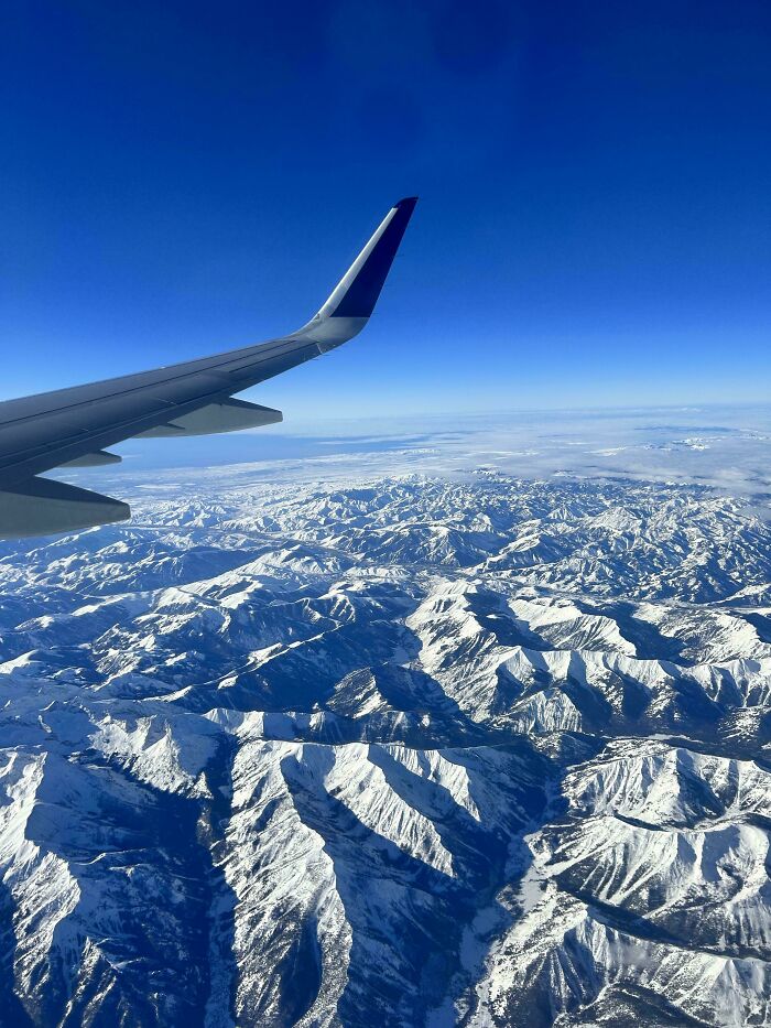 Aerial view of snow-covered mountains from a plane window, showcasing incredible world photos.