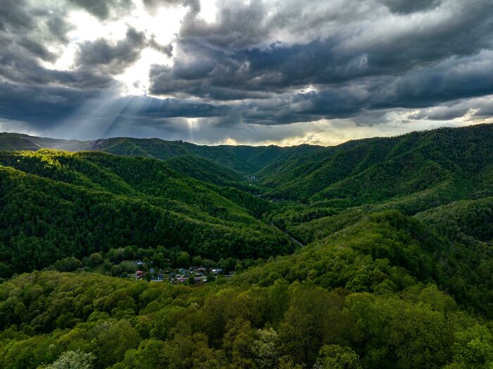 Stunning mountain landscape with dramatic clouds in Incredible World Photos. Sunlight pierces through, highlighting lush greenery.