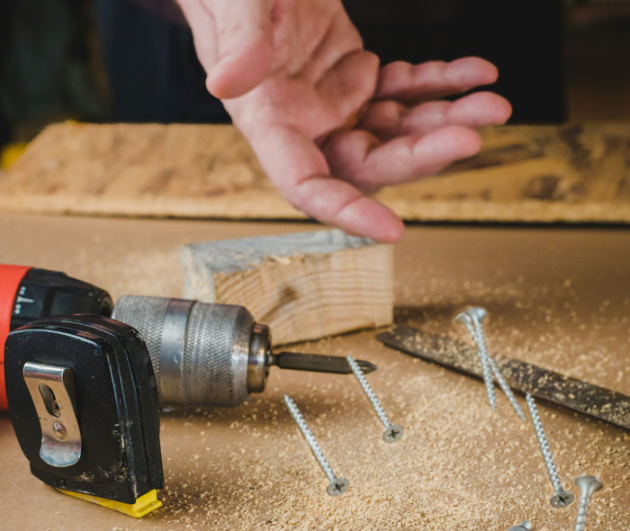 Person handling a drill and screws on a workbench, focusing on security measures and safety practices.