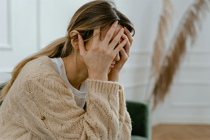 A woman in a beige sweater sits with her head in her hands, representing stress and family tension.