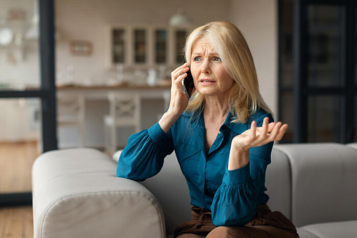 Woman on phone in living room, looking distressed about Christmas situation.