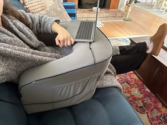 A person using a laptop on a couch with a large cushion, ideal for antisocial people seeking comfort and privacy.