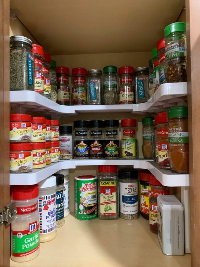 Organized spice cabinet with various labeled jars on tiered shelves.