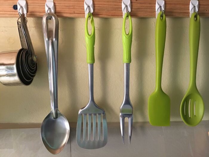 Kitchen utensils with green handles neatly organized on hooks.