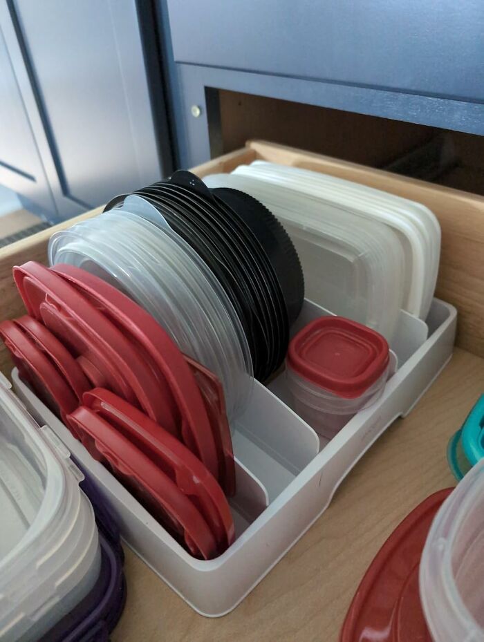 Organized container lids in a cupboard for efficient kitchen storage.