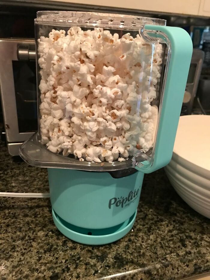 A teal popcorn maker filled with fresh popcorn on a kitchen counter, ideal for antisocial people.