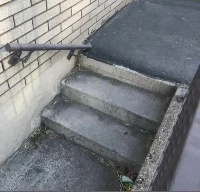 Uneven concrete stairs with a misaligned handrail showing a construction fail.