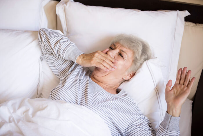 Elderly woman in bed yawning, illustrating unexpected challenges of aging.