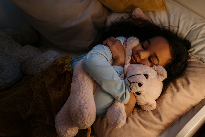 Child peacefully sleeping during holiday season, hugging a teddy bear in a cozy bed.