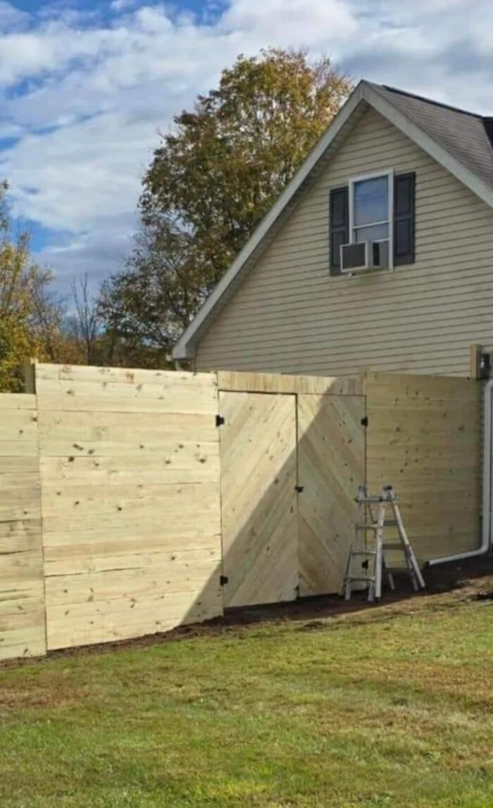 Wooden fence blocking door with a ladder next to it, showcasing a funny construction fail.