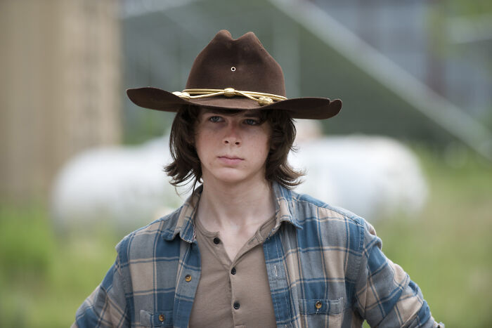 Young person wearing a brown cowboy hat and plaid shirt, representing fascinating fan theories in a rural setting.