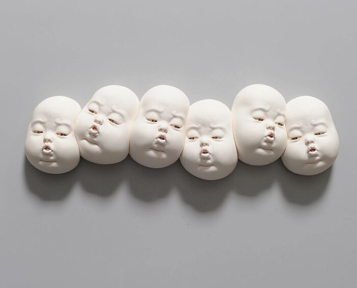 Six expressive sculpted baby faces blend realism and surrealism in an artistic portrayal.