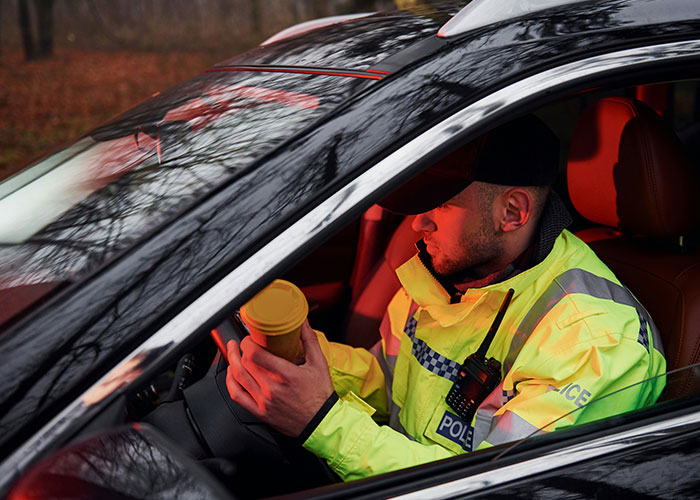 Police officer in car holding a cup, dressed in high-visibility gear, reflecting on wild 911 calls memories.