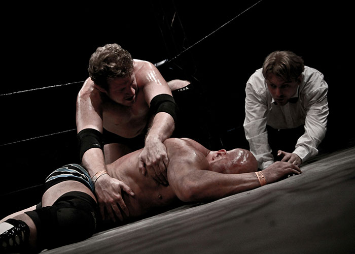 Wrestler pinning opponent in a tense match with referee closely watching.