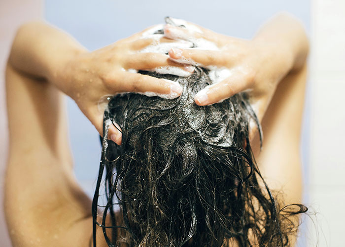 Person washing hair in a shower, covered in soap suds, related to wild 911 calls.