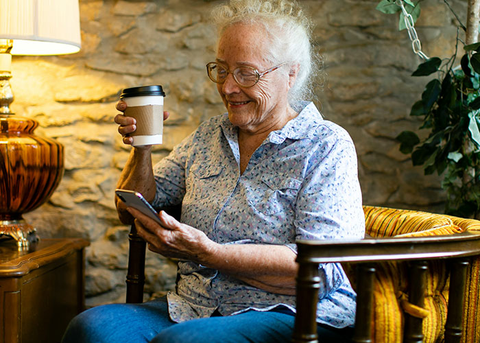 Elderly woman smiling at phone, holding coffee, symbolizing memorable 911 caller.