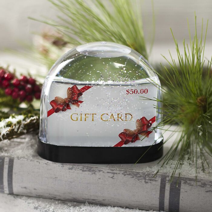 Gift card inside a snow globe with festive decoration on a snowy background.