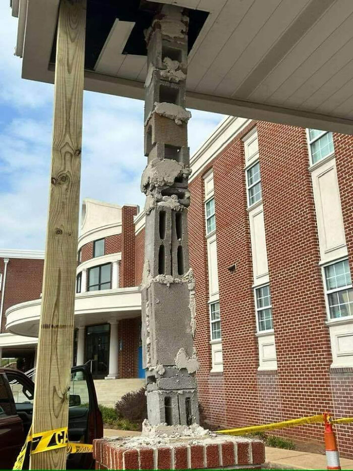 Funny cheap construction fail with crumbling brick column and wooden post for support against a brick building.