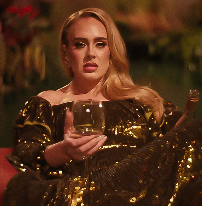 Adele in a glamorous setting, wearing a gold dress, holding a wine glass.