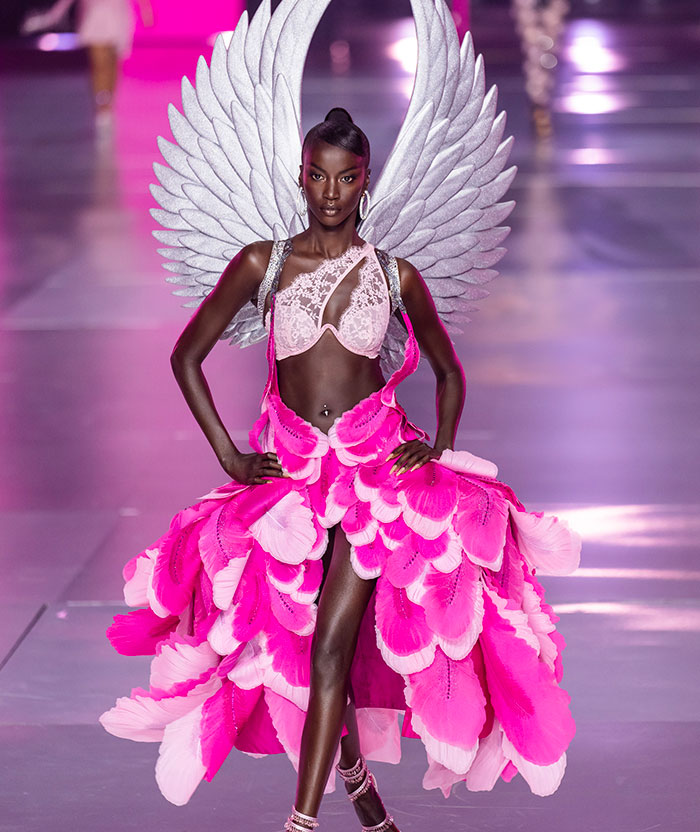 Anok Yai, on Victoria Secret runway in vibrant pink dress with wings, showcasing fashion design.