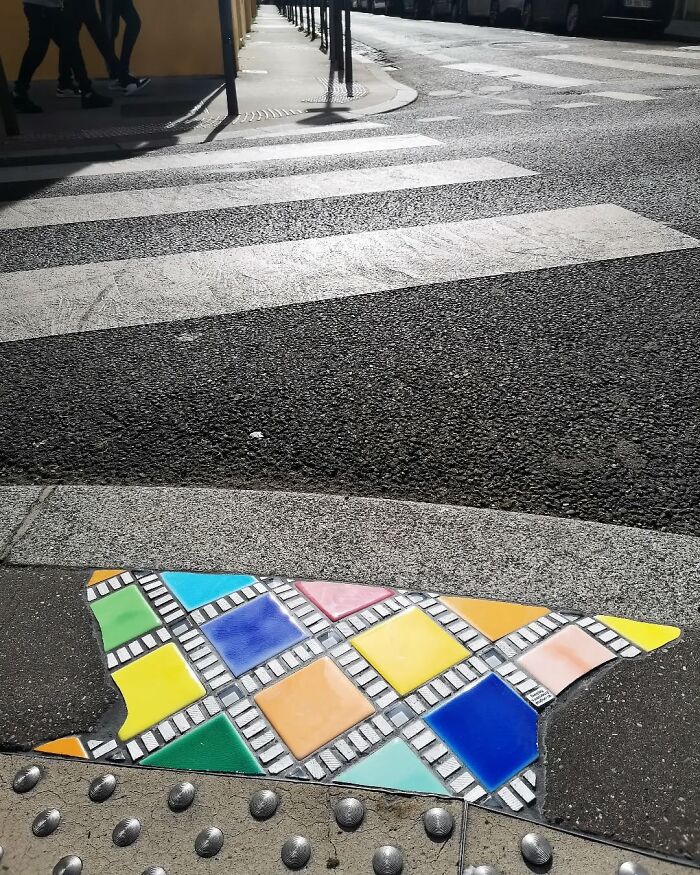 Colorful mosaic art fills a sidewalk crack, enhancing urban scenery.