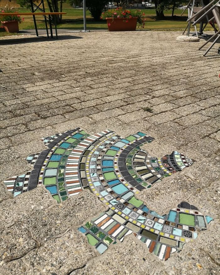 Colorful mosaic artwork fills a crack in a sidewalk, showcasing urban restoration with vibrant patterns.