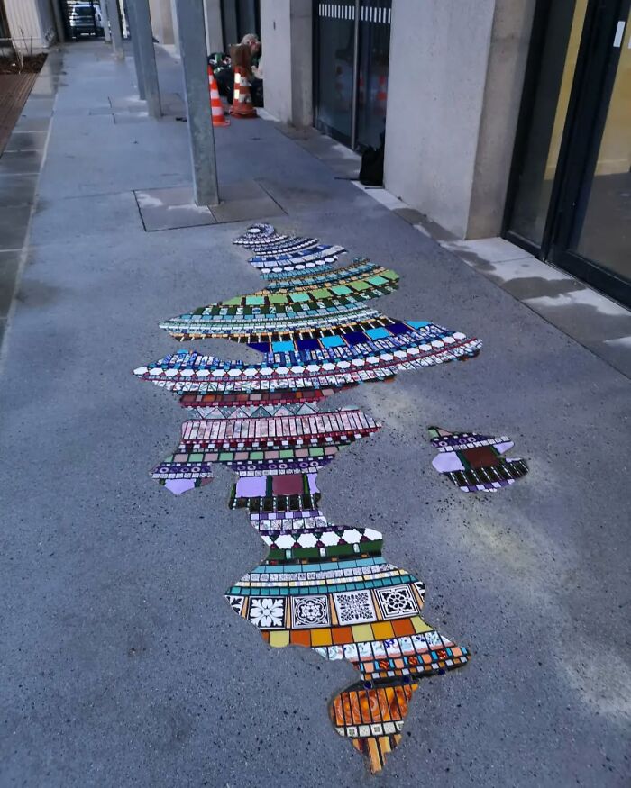 Sidewalk with vibrant mosaic art patching a crack, showcasing colorful and intricate designs.