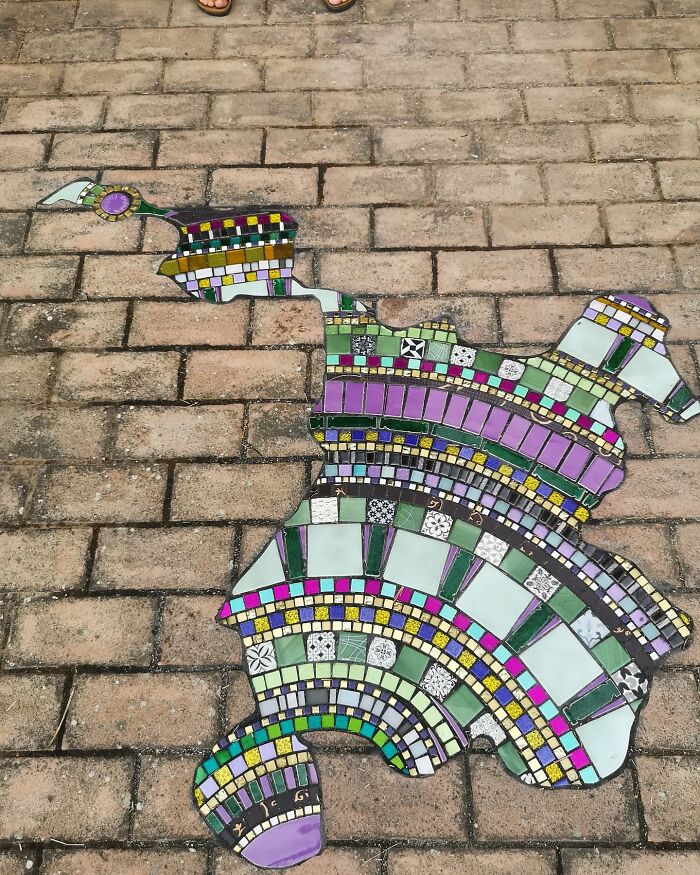 Vibrant mosaic art mending a cracked sidewalk, featuring colorful tiles creating a unique design on the brick pavement.