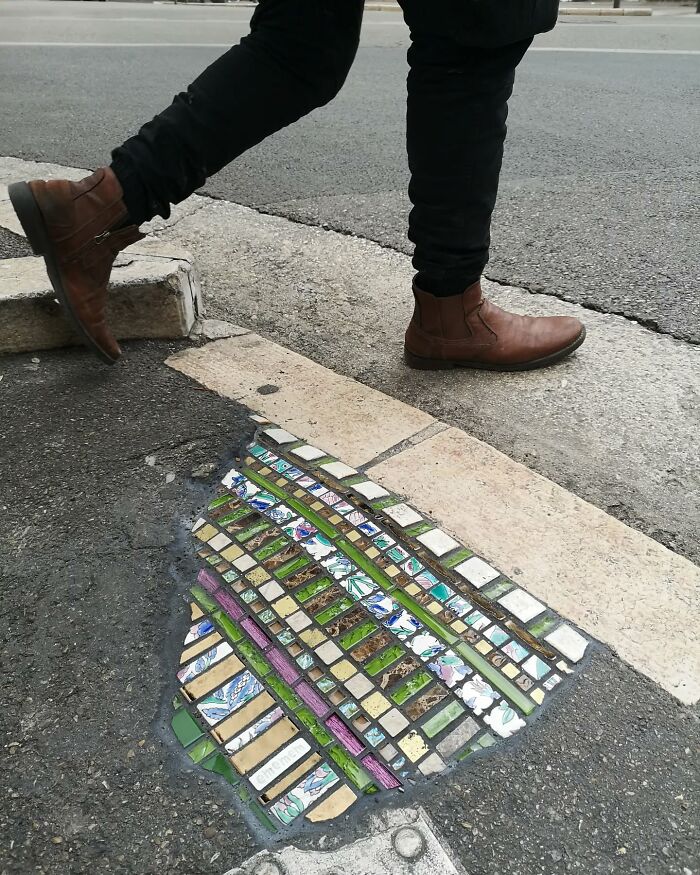 Vibrant mosaic art repairs cracked sidewalk while a person in brown boots walks by.