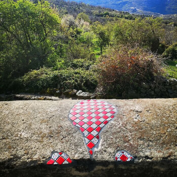 Vibrant mosaic repair on a cracked stone surface with lush green landscape in the background.