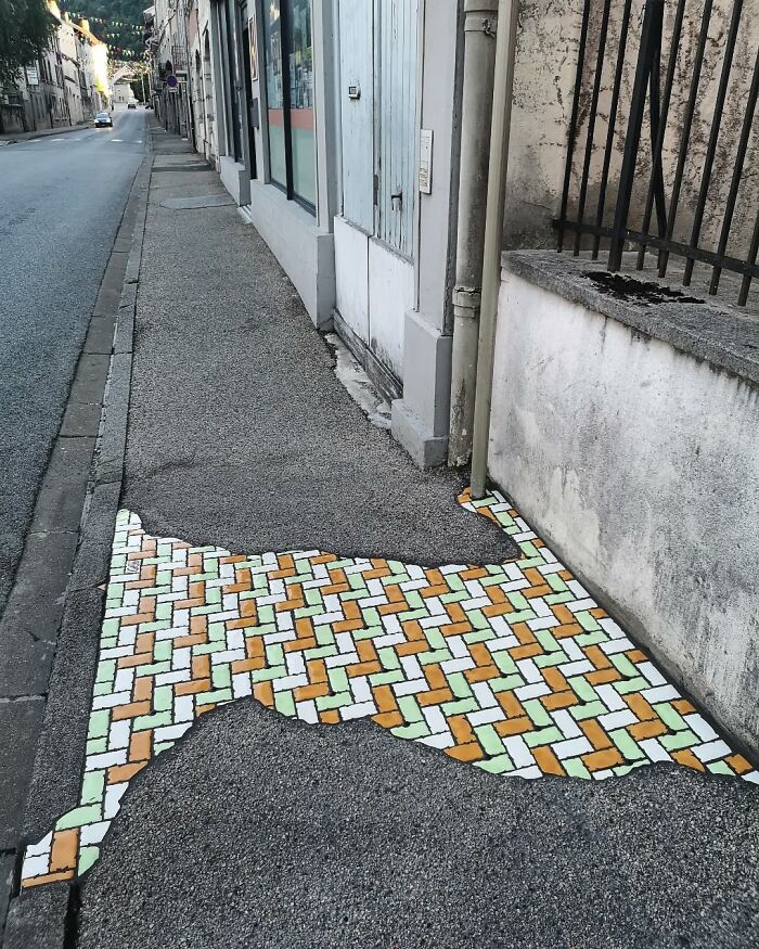 Vibrant mosaic repairs a cracked sidewalk, blending art with urban landscape on a quiet street.