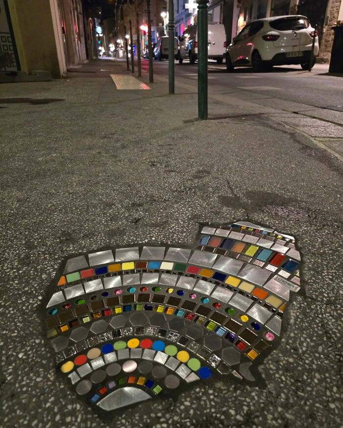 Vibrant mosaic art mending a cracked sidewalk on a dimly lit street at night, with colorful tiles.