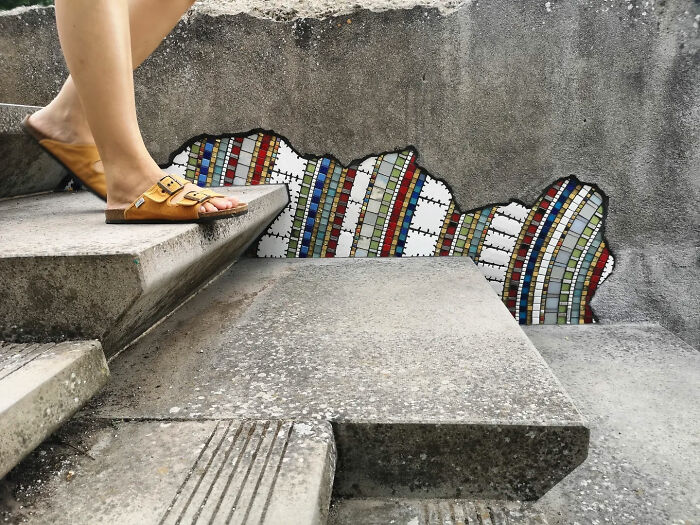 A person walking on stairs with a vibrant mosaic art on a cracked wall.