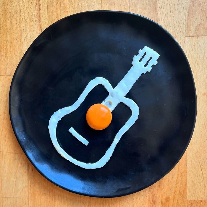 Creative fried egg art shaped like a guitar on a black plate.