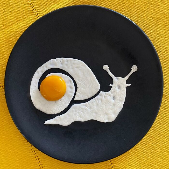 Creative fried egg art shaped like a snail on a black plate, showcasing artistic egg frying techniques.