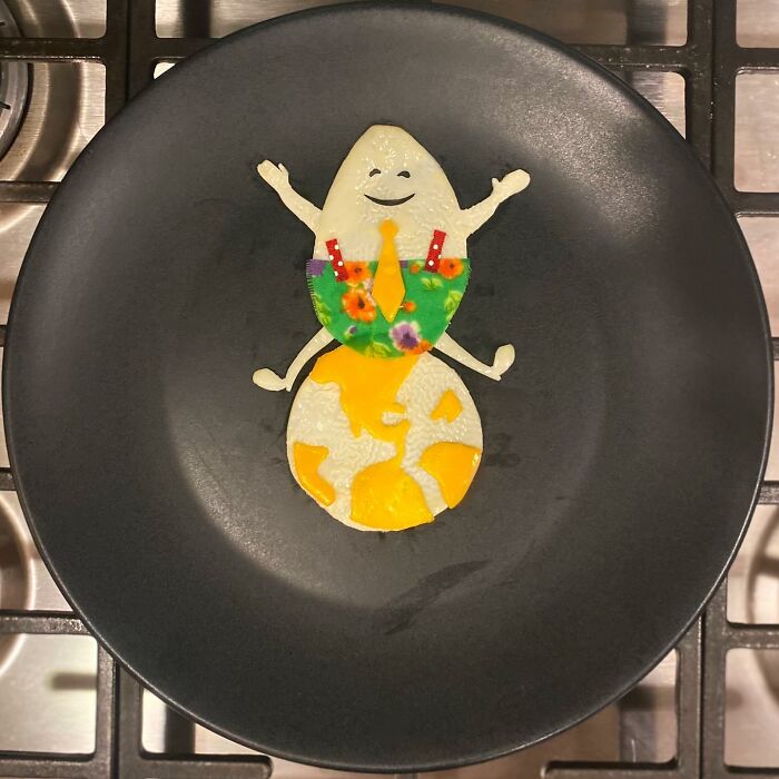 Creative egg art depicting a smiling figure with a colorful outfit on a black plate.