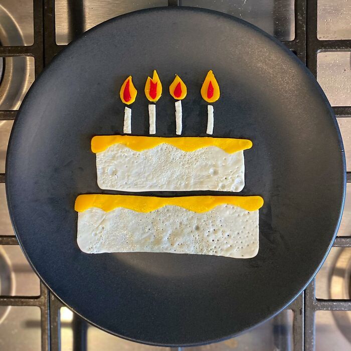 Creative egg art resembling a cake with candles on a black plate.