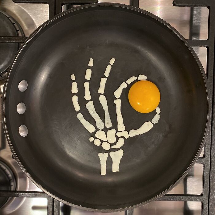 Creative egg art with yolk as sun and white as skeleton hand in frying pan.