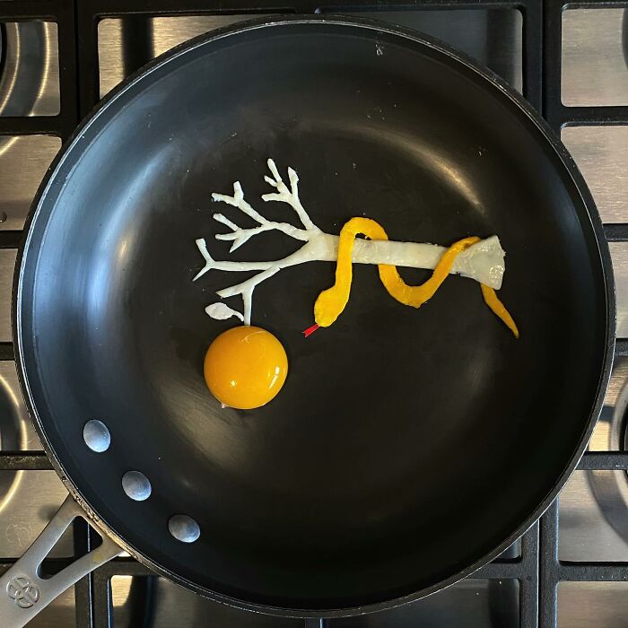 Creative egg art depicting a snake and branch design in a frying pan.