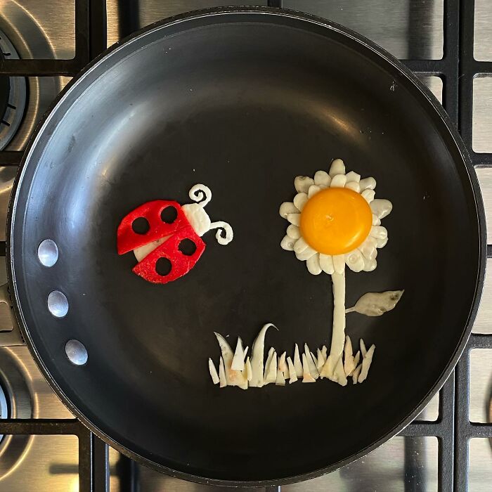 Creative fried egg art with a sunny-side-up flower and pepper ladybug in a pan.