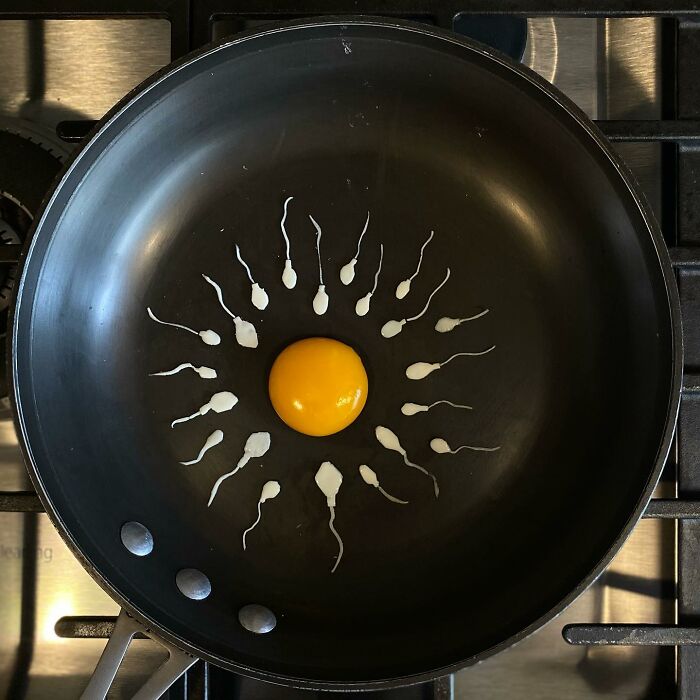 Creative egg art in frying pan with yolk surrounded by sperm shapes.