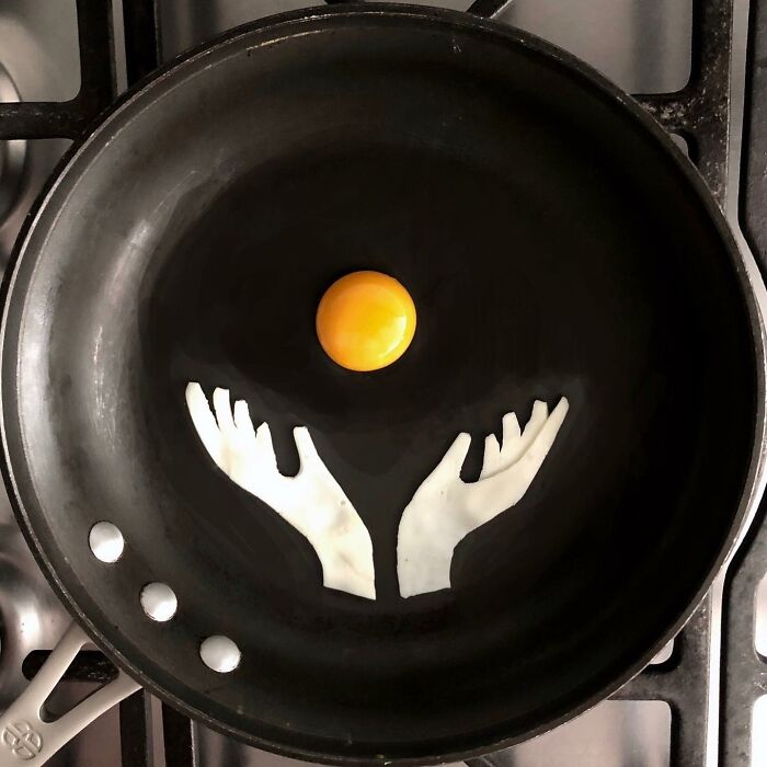 Creative egg art with yolk as sun and whites shaped like hands in a frying pan.